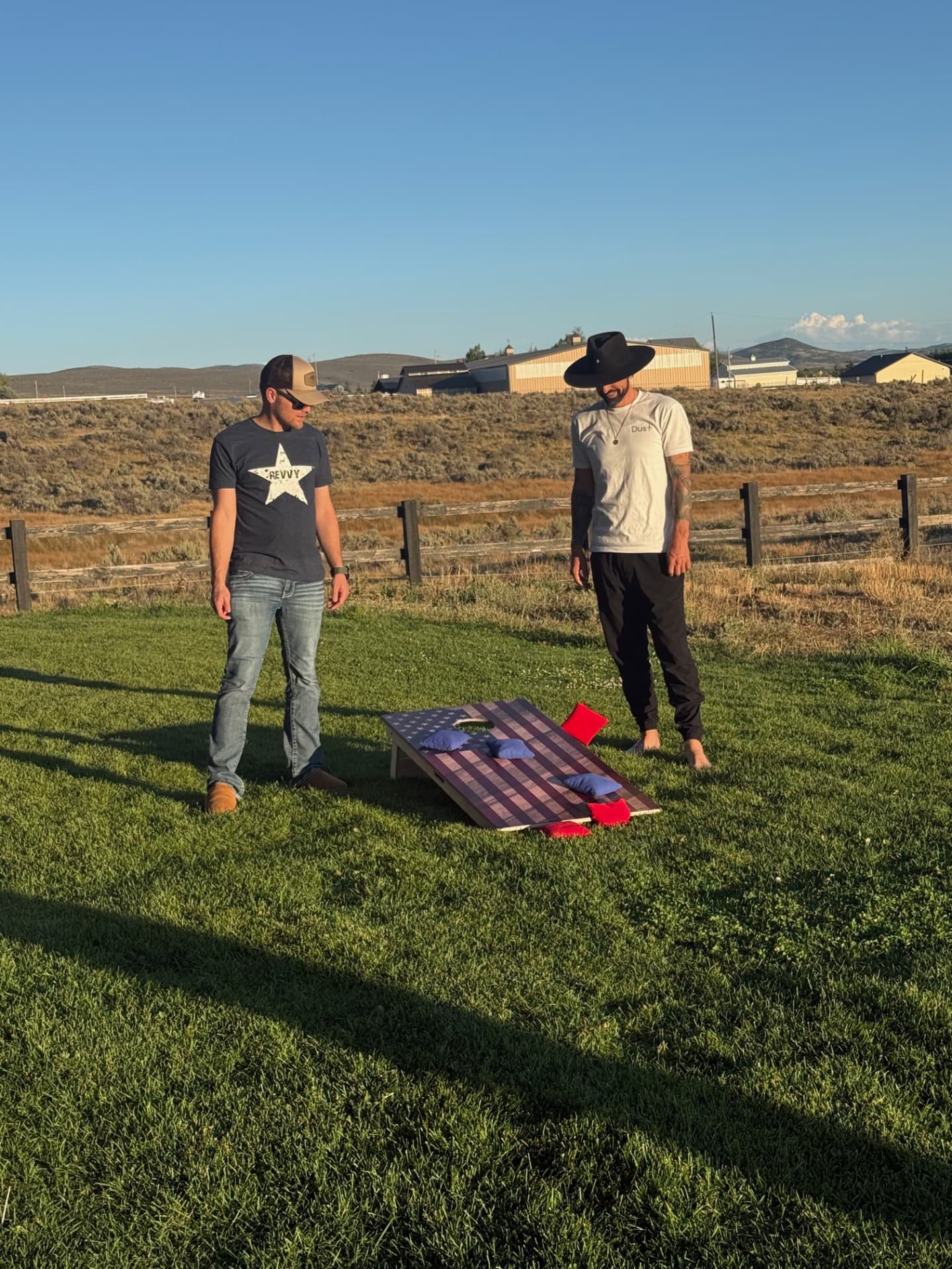 Two participants playing cornhole on the lawn at golden hour